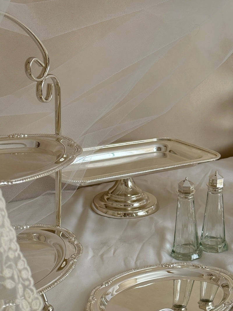 Set of silver platters and glass salt and pepper shakers on a white surface.