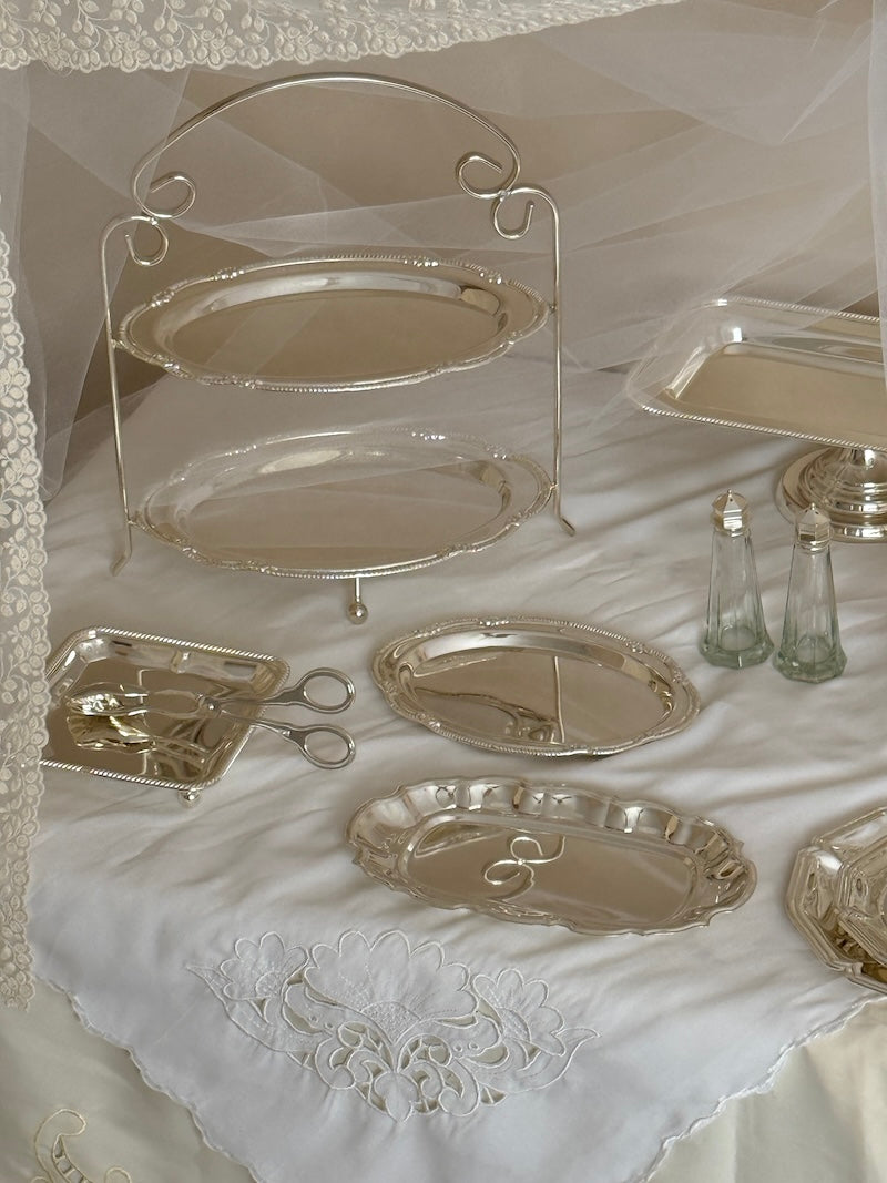 Collection of silver platters and a stand on a white lace tablecloth.