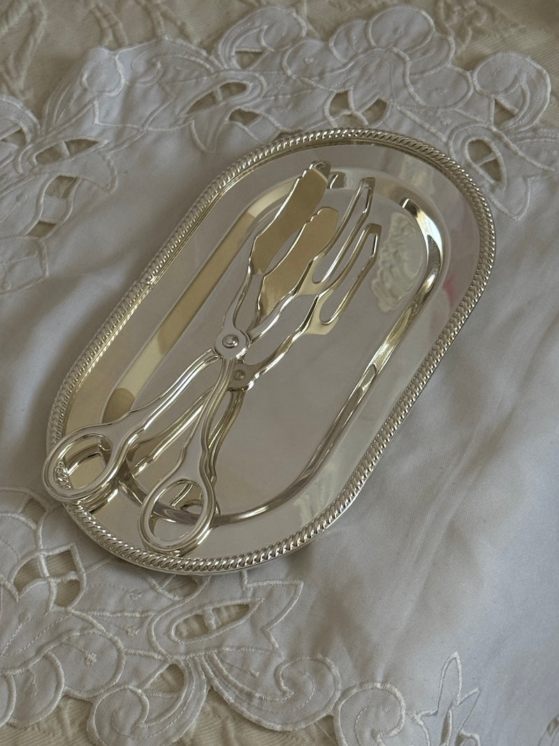 Silver tongs on a decorative silver tray with lace background