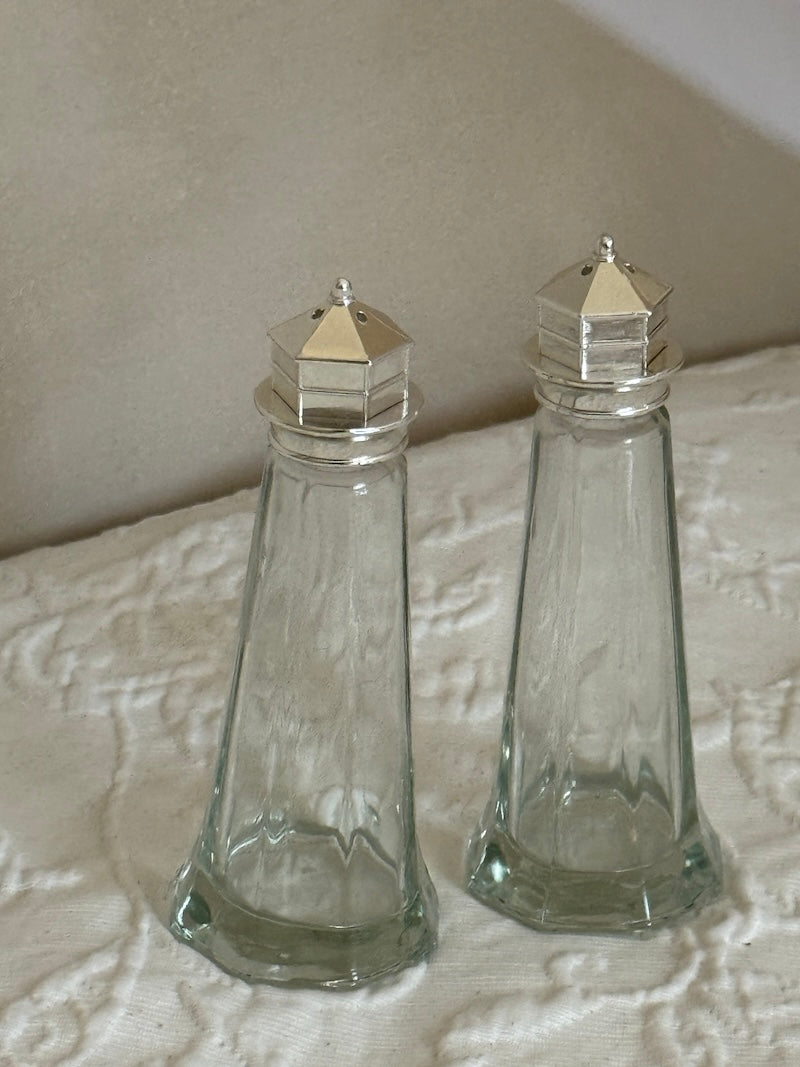 Two clear glass salt shakers with silver tops on a textured surface.