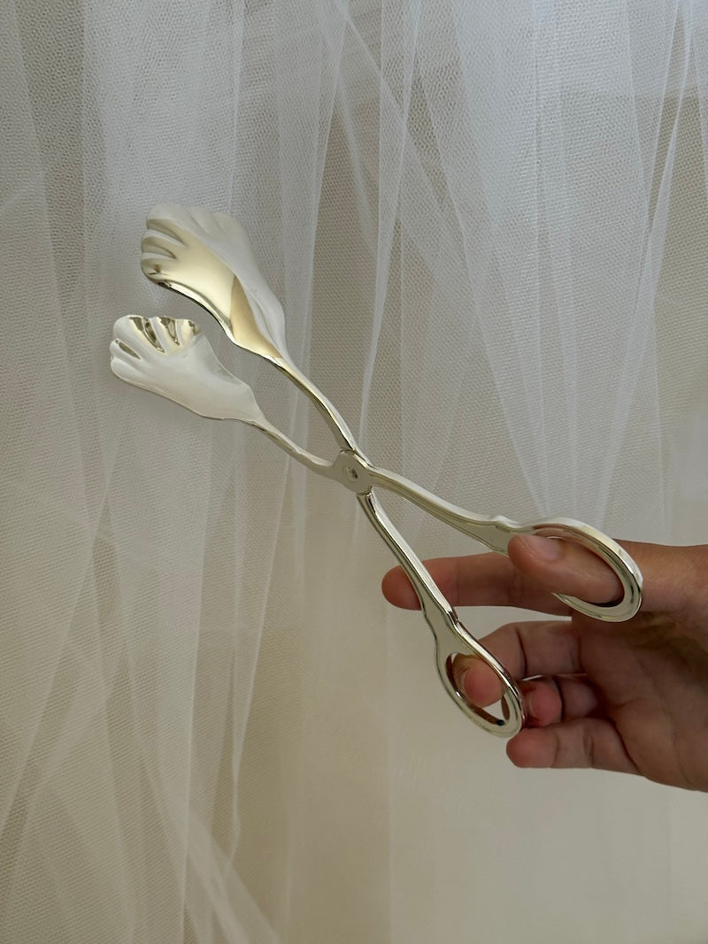 Metallic tongs held by a hand against a sheer white curtain background