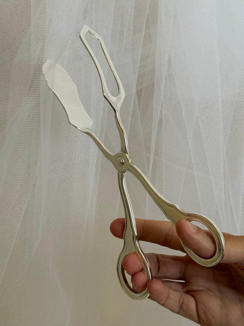 silver tongs held by a hand against a sheer white curtain background