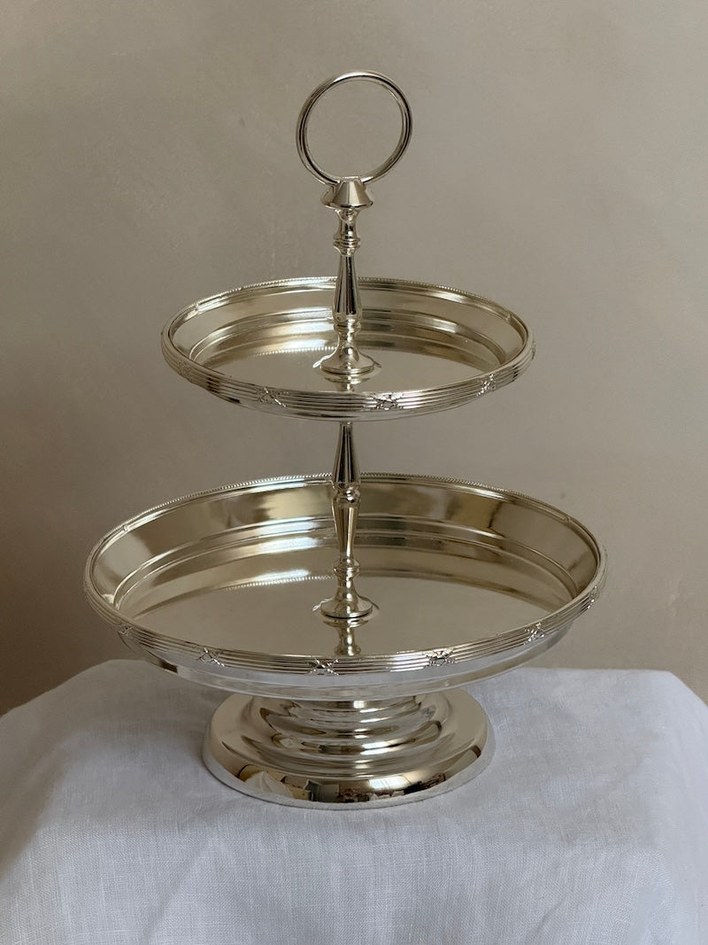 Silver two-tiered stand on a white surface with a neutral background