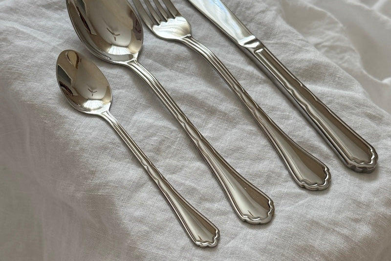Set of silver cutlery including a knife, fork, and two spoons on a white fabric background.