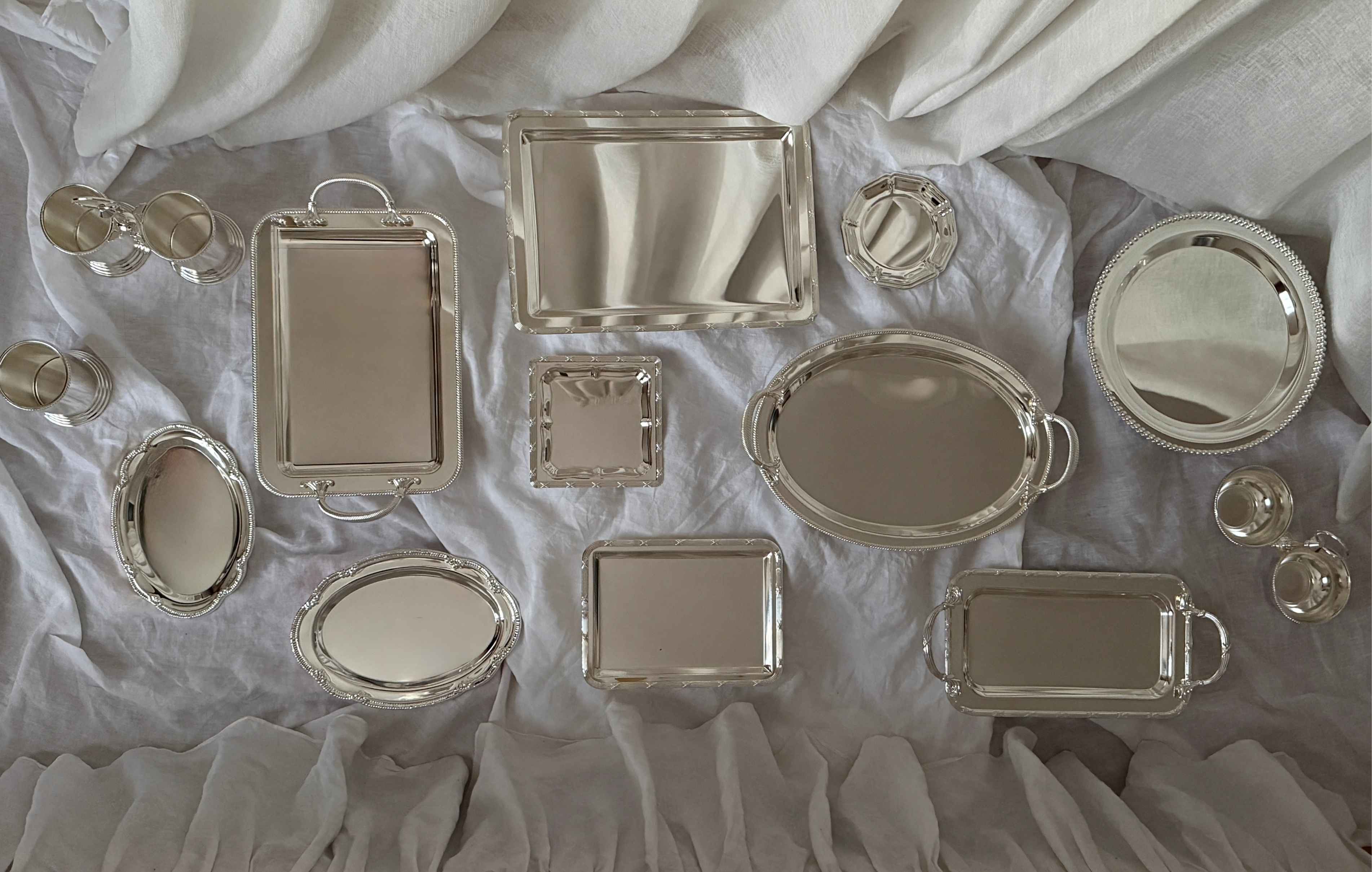 Collection of silver trays and decorative items on a white fabric background
