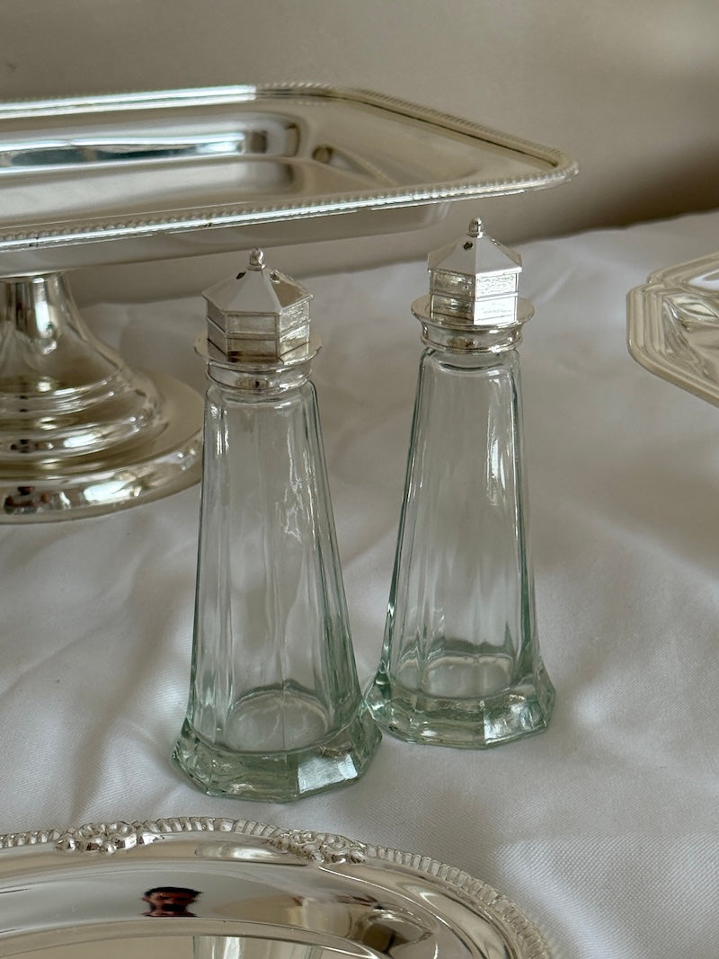 Clear glass salt and pepper shakers with silver lids on a white tablecloth.