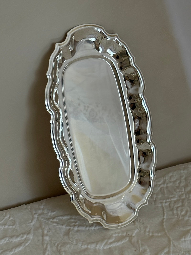 Silver decorative tray on a textured surface with a neutral background