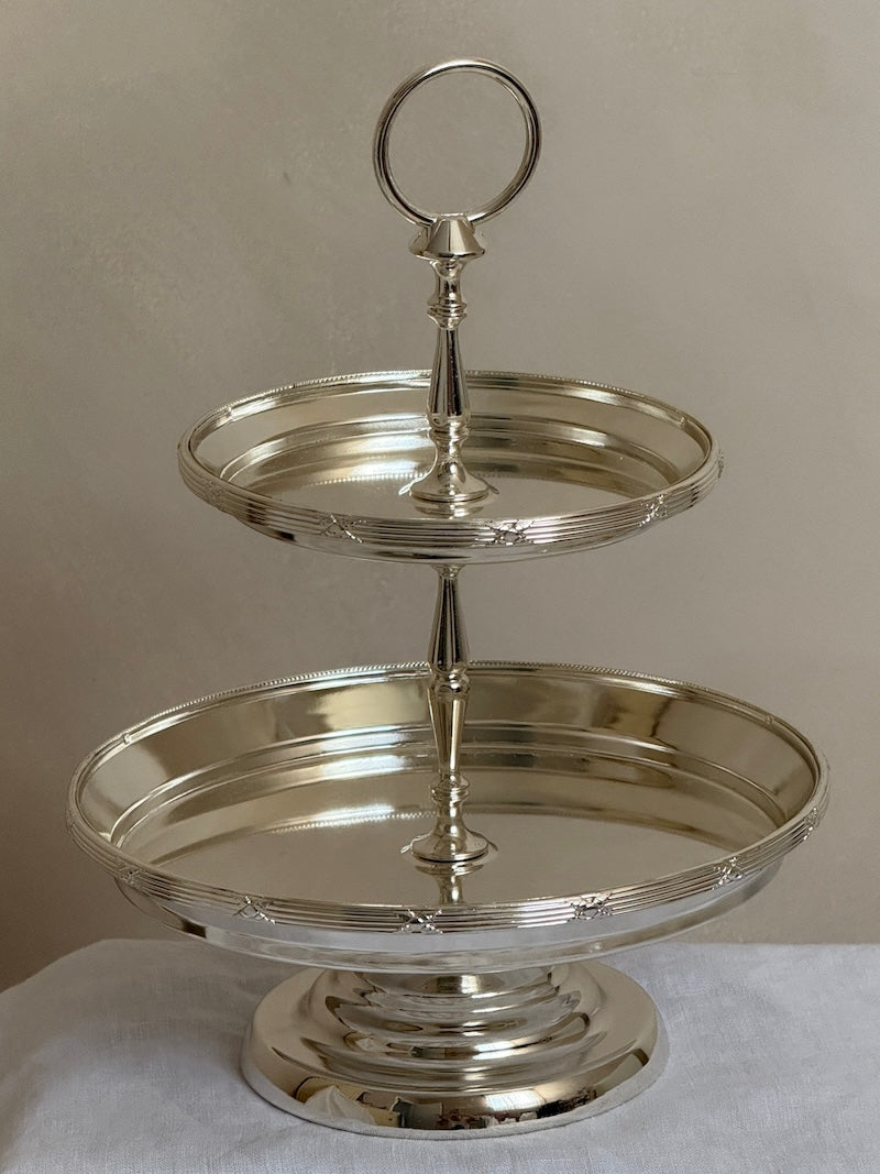 Silver two-tiered stand on a white surface with a neutral background