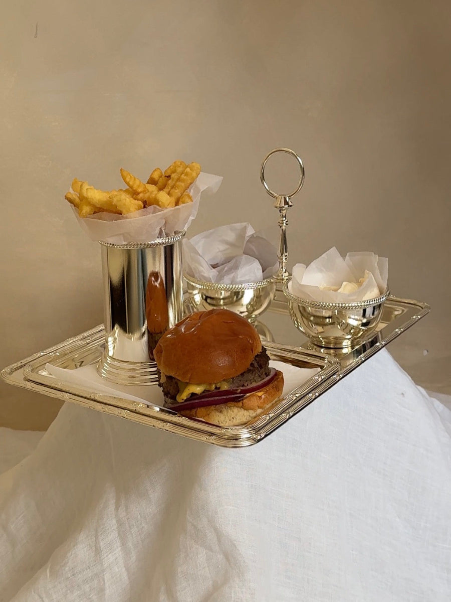 Tray with a burger, fries, and side dishes on a neutral background